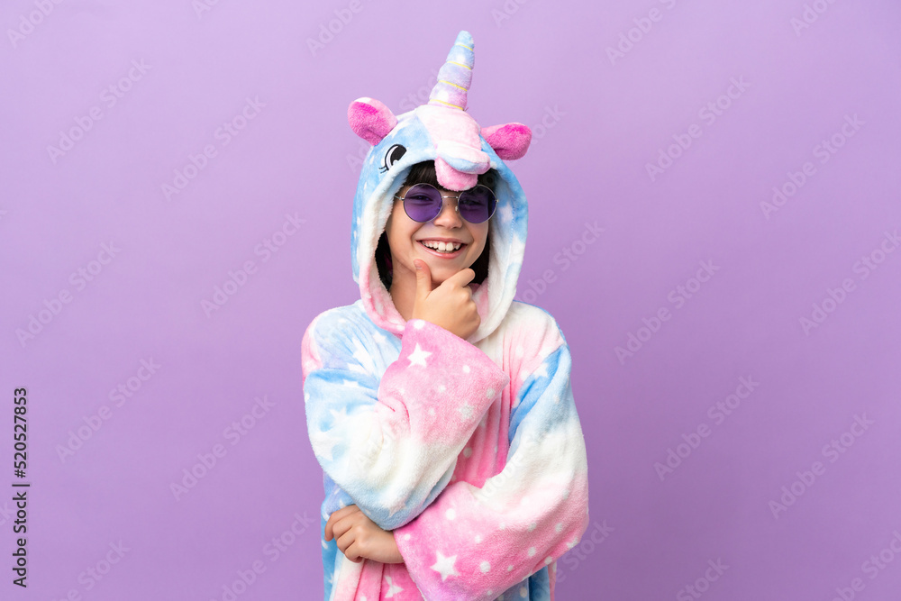 Little kid wearing a unicorn pajama isolated on purple background with glasses and smiling