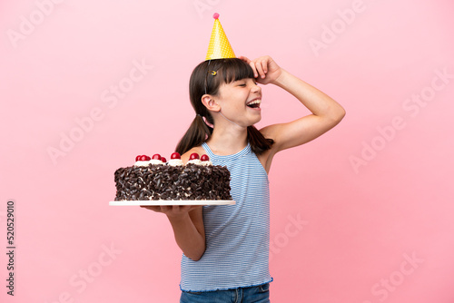 Little caucasian kid holding birthday cake isolated in pink background smiling a lot