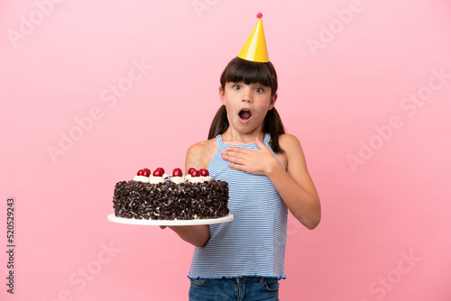 Little caucasian kid holding birthday cake isolated in pink background surprised and shocked while looking right