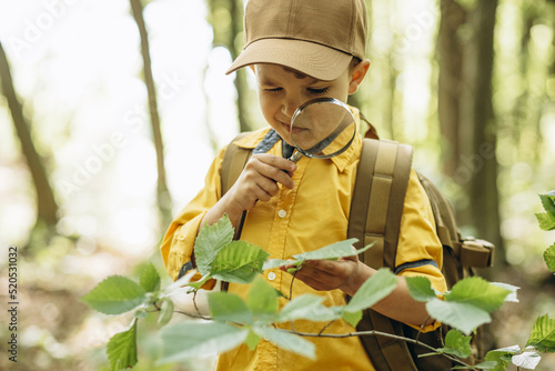 Boy traveler looking through magnifying glass in the forest photo