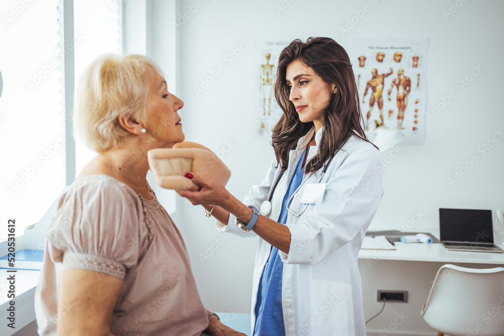 Portrait of a female doctor helping a senior woman at office with her neck injury and putting her collar a healthcare and medicine concepts. Doctor putting a neck brace on a senior patient Portrait of a female doctor helping a senior woman at office with her neck injury and putting her collar a healthcare and medicine concepts. Doctor putting a neck brace on a senior patient