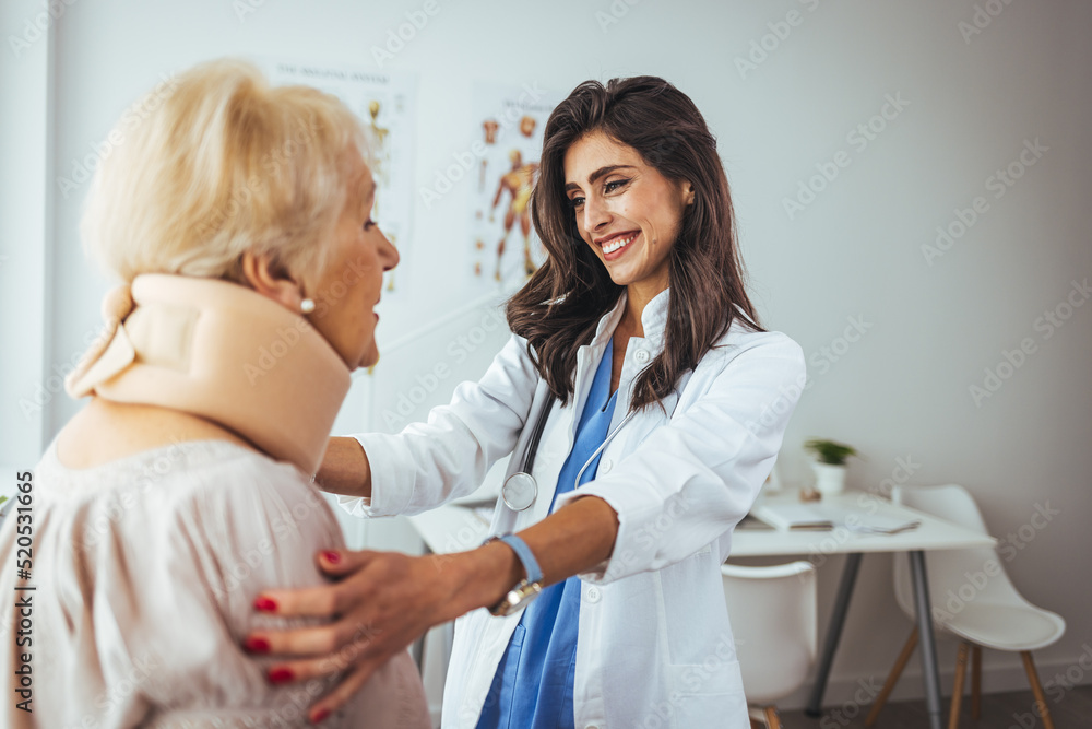 Young woman with injury of neck visiting doctor in clinic. Doctor examining a patient at desk in medical office. Doctor talking to a senior patient with cervical collar at the hospital Young woman with injury of neck visiting doctor in clinic. Doctor examining a patient at desk in medical office. Doctor talking to a senior patient with cervical collar at the hospital