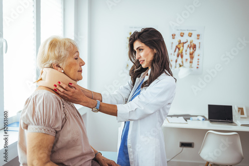 Female doctor putting neck orthopaedic collar on adult injured woman. Picture of senior woman having a visit at female doctor's office. Doctor helping a senior woman with her neck injury