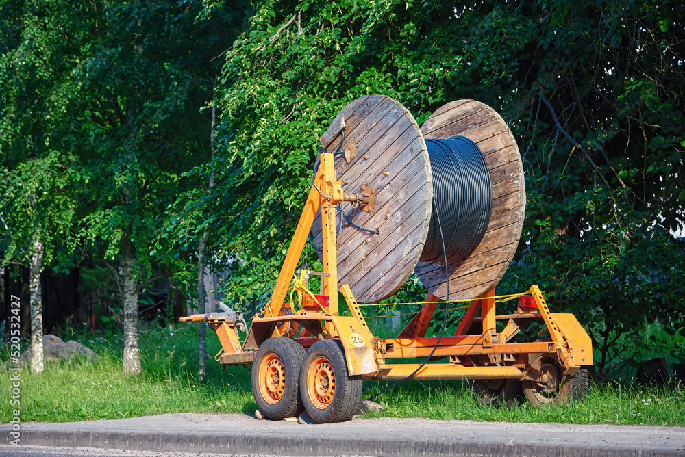 Wooden reel with fiber optic cable mounted on trailer for easy transportation. Laying optical fiber cable in suburb, fast internet concept. Cabling, laying of underground communications.