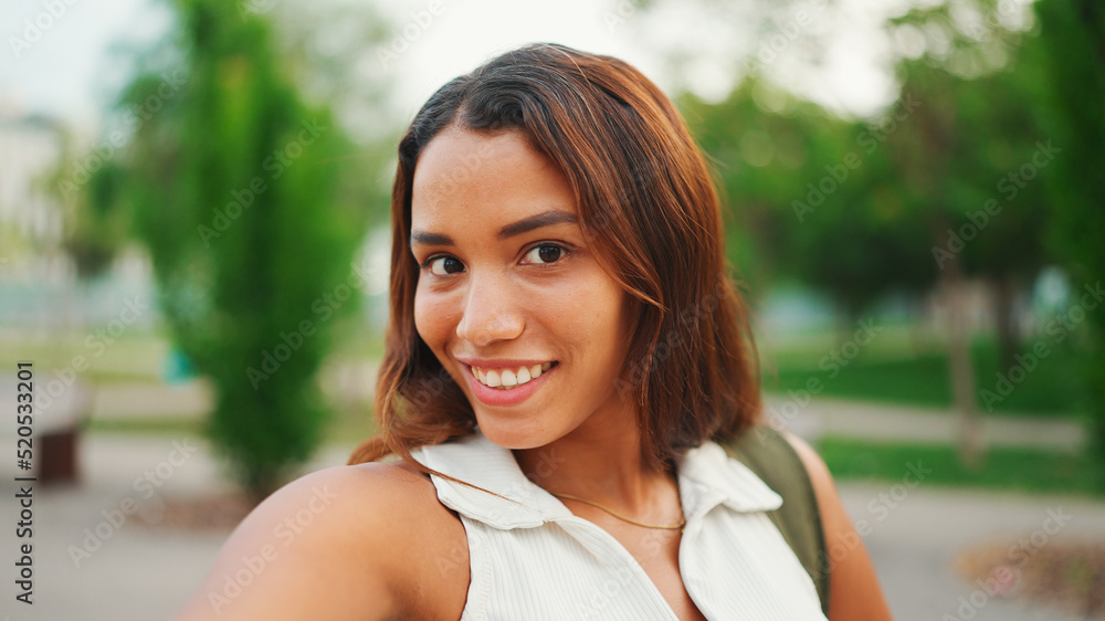 Lovely girl with brown long hair, tanned skin wearing white top is using mobile phone. Smiling young woman taking selfie on cellphone Lovely girl with brown long hair, tanned skin wearing white top is using mobile phone. Smiling young woman taking selfie on cellphone