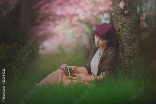 A young woman with purple hair sitting in a flowering orchard playing the kalimba - a musical instrument with a wooden soundboard and metal keys. photo