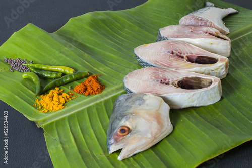 Raw hilsa fish cut into pieces kept on banana leaf for cooking. Shot taken in studio with copy space background and spices. photo