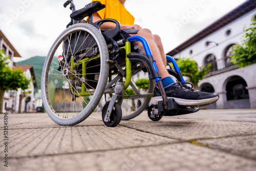 Detail of a disabled person in a wheelchair walking through the town square © unai