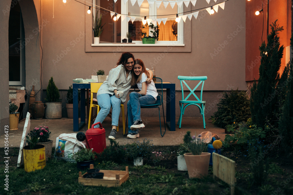 mother with her daughter sitting in backyard while gardening houseplants