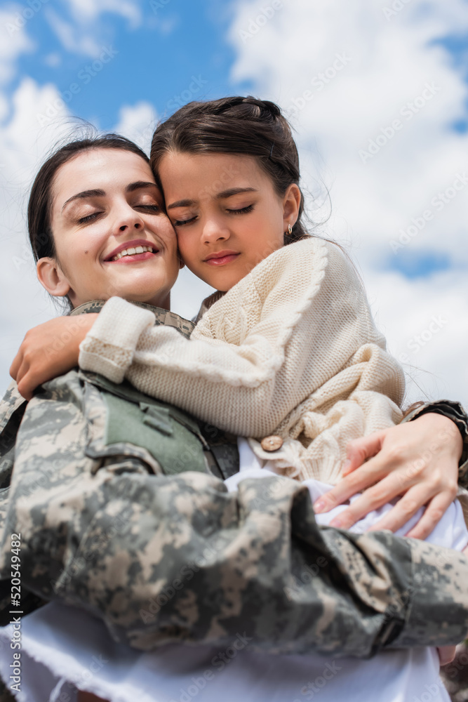 smiling military woman with closed eyes embracing daughter against cloudy sky smiling military woman with closed eyes embracing daughter against cloudy sky