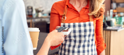 Close Up Of Female Customer In Coffee Shop Making Contactless Payment With Card