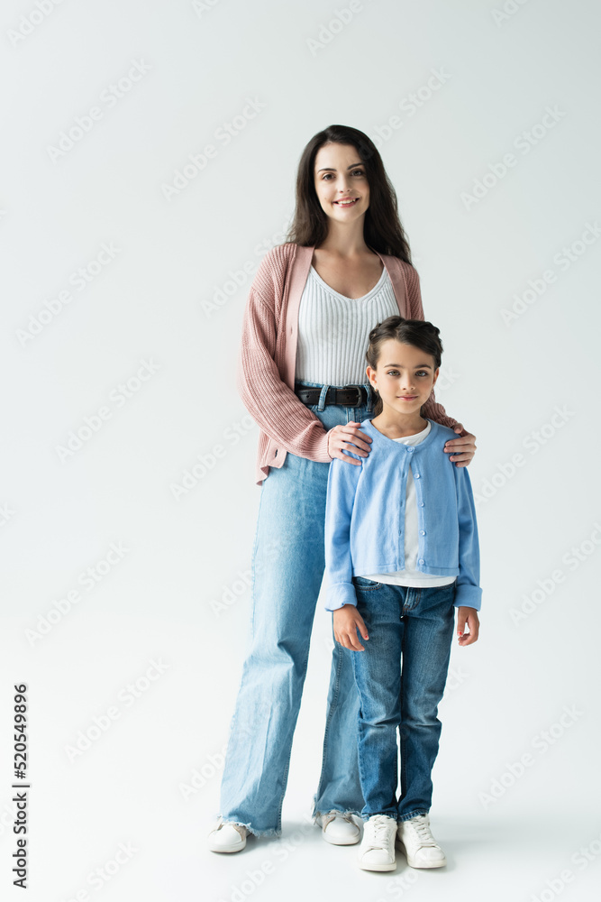 full length of positive woman with daughter in jeans standing on grey background full length of positive woman with daughter in jeans standing on grey background