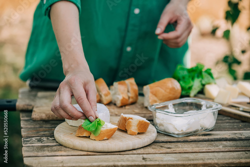 Stylish woman in green shirt make a snack with bread and cheese on a table in outdoor