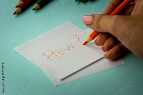 Women's hand writing how on a piece of paper with some other pencils in the background photo