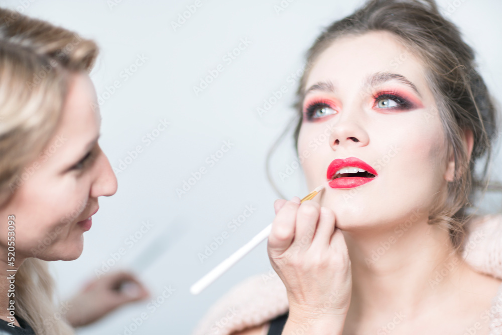 Makeup artist applies red lipstick. Beautiful female face. Close-up. Makeup artist applies red lipstick. Beautiful female face. Close-up.