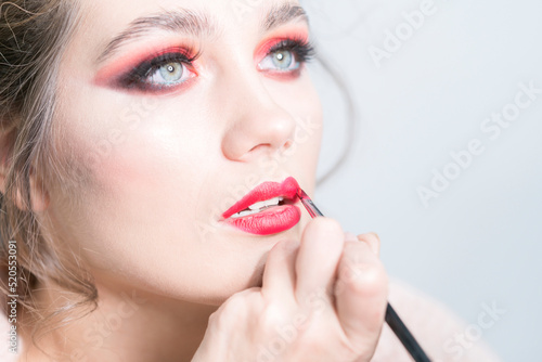 Makeup artist applies red lipstick . Beautiful woman face. Hand of make-up master  painting lips of beauty model girl.