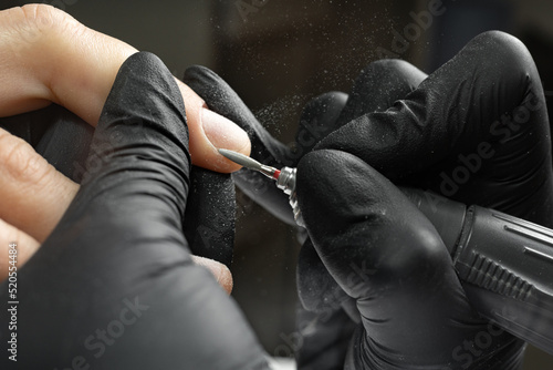 Close-up of manicurist uses an electric drill to remove old gel polish from nails. A woman is getting a manicure of nails. The beautician files client s nails. professional manicure tool.
