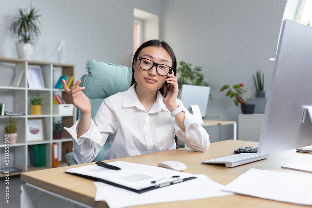 Online sales. A young beautiful Asian woman sales manager sells goods on the phone, calls customers, talks on the phone. Sitting at a desk in a modern office. Online sales. A young beautiful Asian woman sales manager sells goods on the phone, calls customers, talks on the phone. Sitting at a desk in a modern office.
