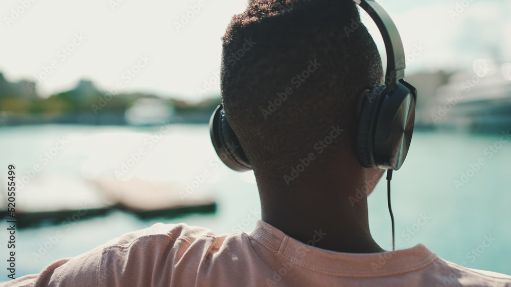 Clouse up, young african guy relaxes sitting on bench in the port on yachts and ships background. Back view Clouse up, young african guy relaxes sitting on bench in the port on yachts and ships background. Back view