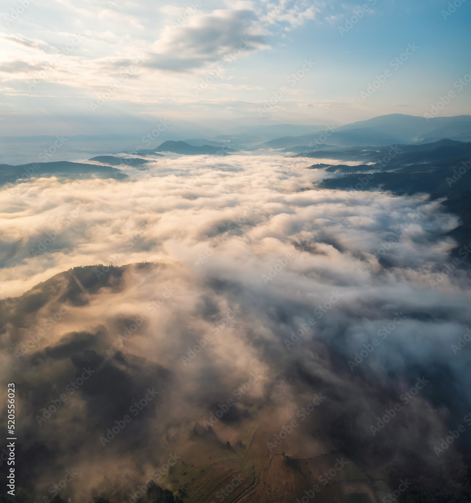 Amazing aerial view of beautiful low clouds creeping on the tree-covered mountain slopes, the Rhodopes in Bulgaria at sunrise.