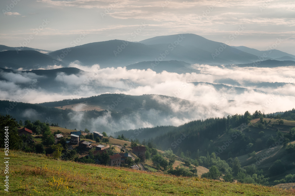 Amazing view with small mountain huts against the background of beautiful low clouds creeping among the mountain slopes, Rhodopes in Bulgaria at sunrise
