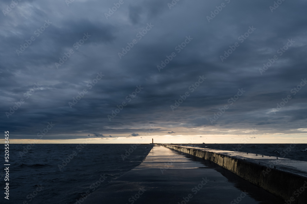 Scenic landscape of sunset over Baltic sea. Cloudy sky. Mangalsala mols. Way to lighthouse. Dramatic seascape.