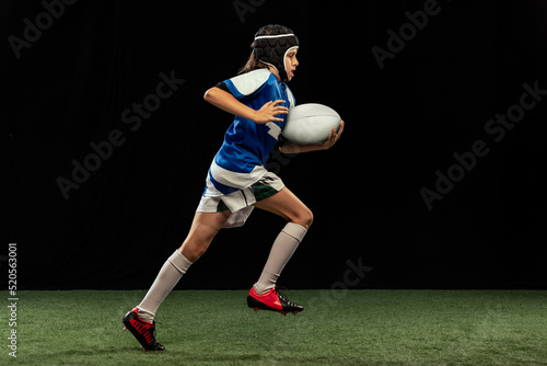 Εκτύπωση καμβά Dynamic portrait of school age boy, junior male rugby player practicing rugby football isolated on dark background with grass floooring