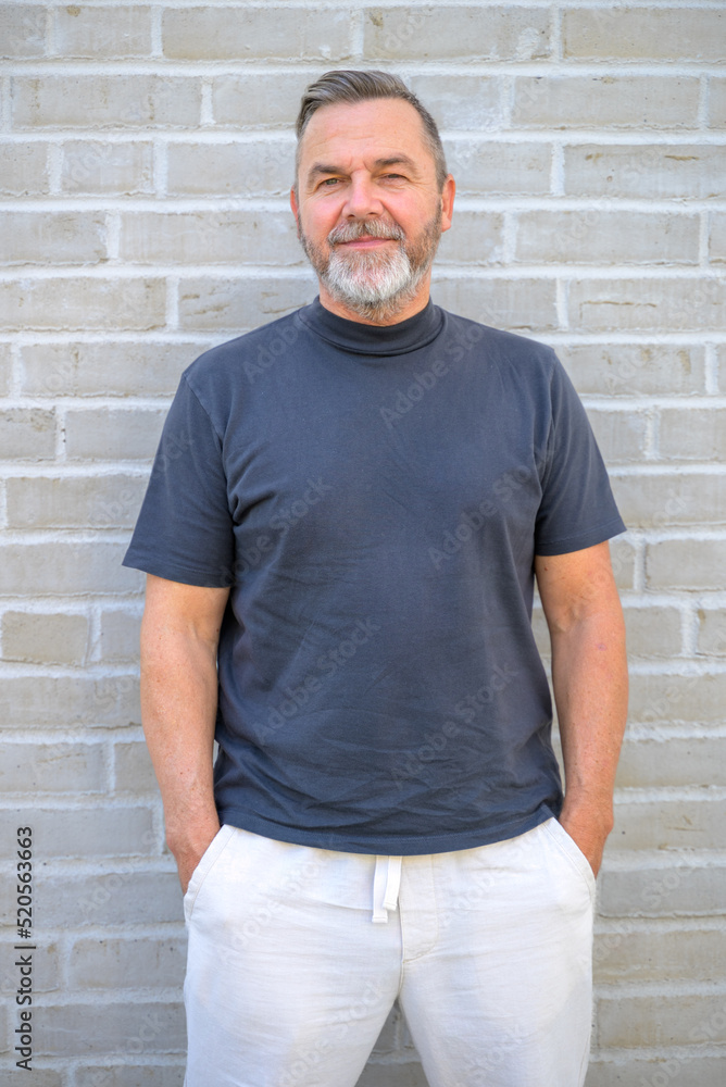 Trendy senior man posing looking aside in front of brick wall