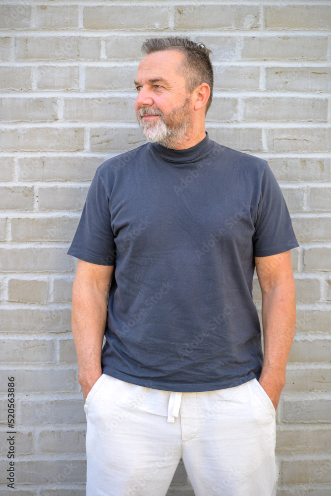 Trendy senior man posing looking aside in front of brick wall Trendy senior man posing looking aside in front of brick wall