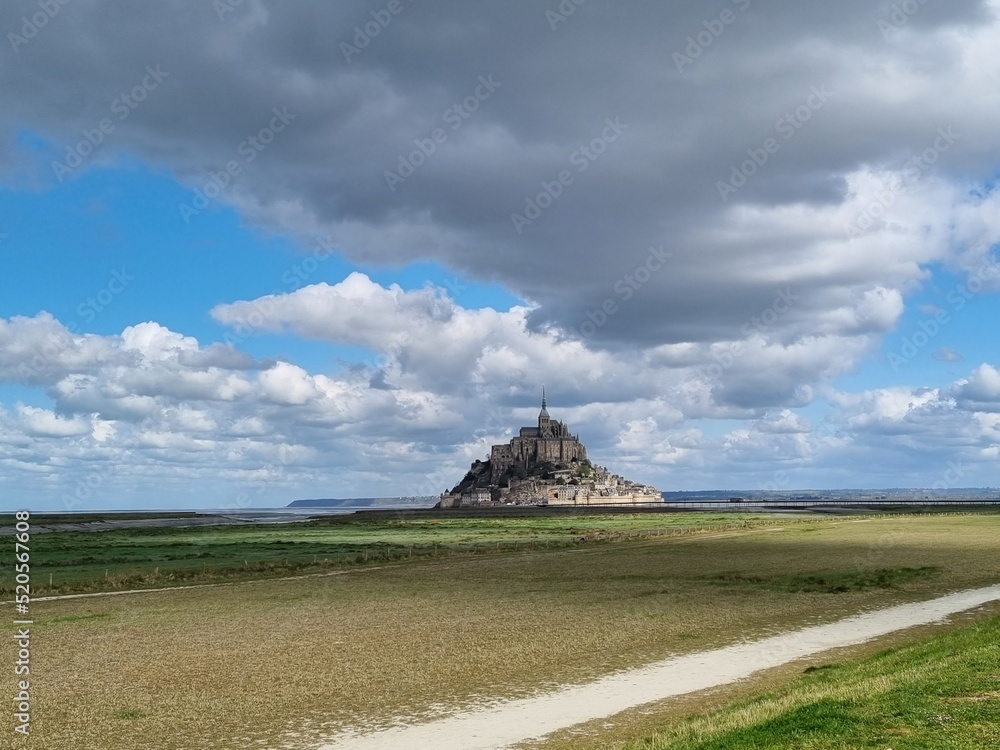 Distant view of Mont Saint Michel with dramatic cloudscape and grassy meadows in front Distant view of Mont Saint Michel with dramatic cloudscape and grassy meadows in front