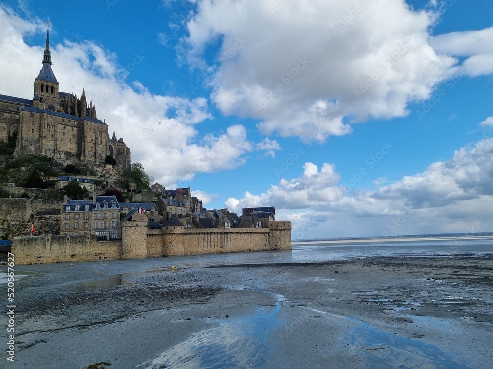 Distant view of Mont Saint Michel at low tide, surrounded by sand and dramatic cloudscape