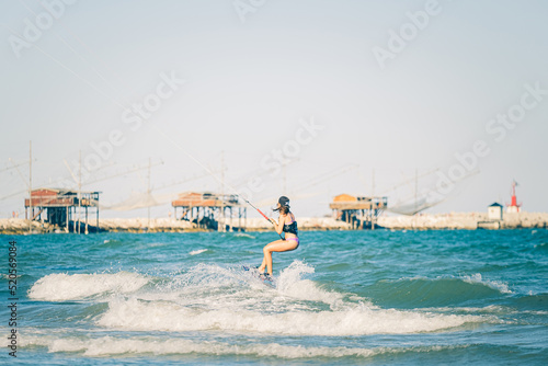 Kite surfing girl in swimsuit with kite in the sky rides the waves with splashing water. Water sports, sporty woman, action concept and hard sport