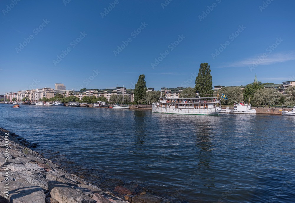 Naklejka premium Apartment houses at the water front districts Nacka and Hammarby sjöstad, Canal boat Diana passing for the town Göteborg a sunny summer day in Stockholm