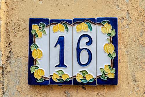 Ceramic background. Italian traditional patterns on tiles, handmade craft painting - numbers for apartments and houses. Number sixteen 16 with lemons.
