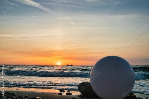 Fototapeta Close-up of a pink balloon on a rocky beach with sea waves in the background, Is