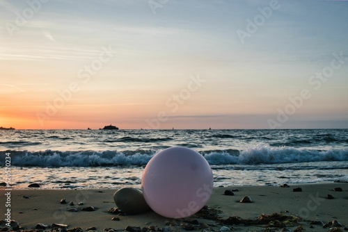Fotografie, Obraz Pink balloon on a rocky beach during evening with sea waves in the background, I