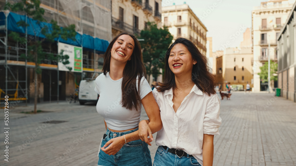 Young multiethnic women walk laughing down the street on warm summer day on the old town background