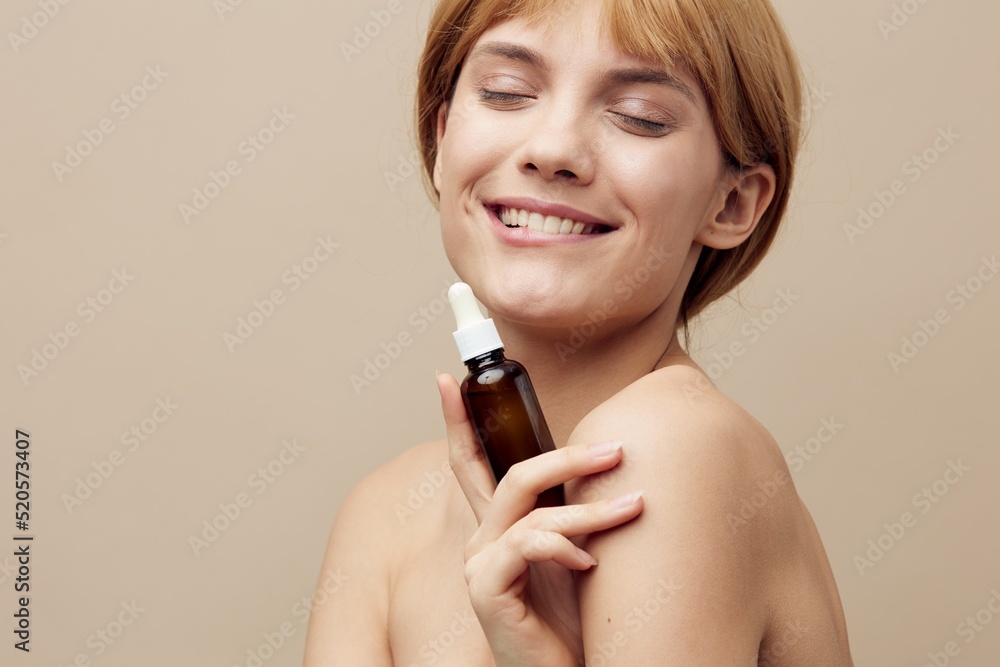 Close-up photo. Horizontal studio shot.A nice woman in a towel with white well-groomed skin, short red hair on a beige background with a new serum is studying its composition and properties. Close-up photo. Horizontal studio shot.A nice woman in a towel with white well-groomed skin, short red hair on a beige background with a new serum is studying its composition and properties.