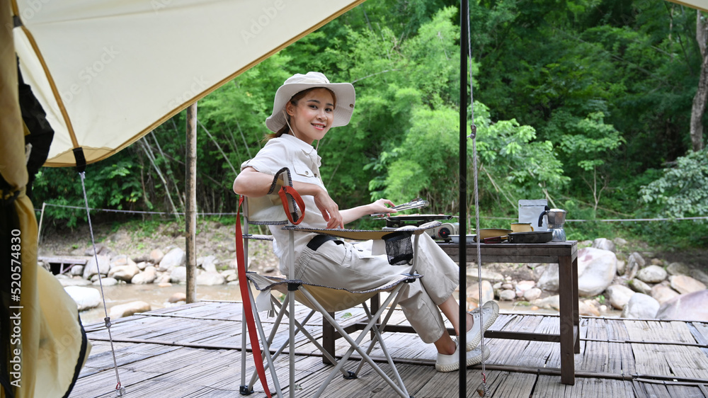 Young woman tourist sitting on folding chair near camping tents. Travel, adventure and vacation concept Young woman tourist sitting on folding chair near camping tents. Travel, adventure and vacation concept