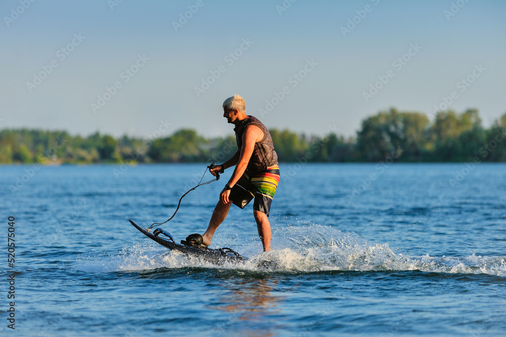 A professional wakeboarder rides on the lake in sunny weather, performing figures A professional wakeboarder rides on the lake in sunny weather, performing figures