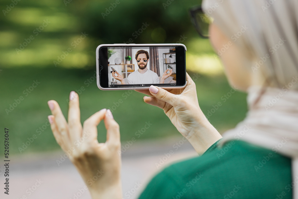 Young muslim woman, resting at park with digital smart phone, having a video call with her friend, handsome bearded man, showing his care routine with eye patches.