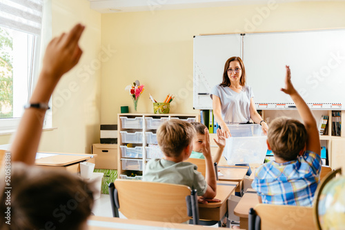 Save the earth. Charming female teacher with small school children in classroom learning about waste separation. Children raised their hands to answer, rear view.