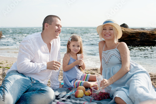 Young family have a rest near sea, happy parents with daughter make a picnic
