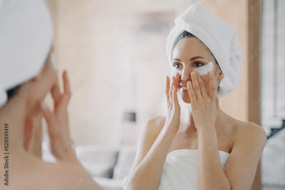 Girl applies eye patches and looking into mirror. Attractive woman wrapped in towel after bathing. Girl applies eye patches and looking into mirror. Attractive woman wrapped in towel after bathing.
