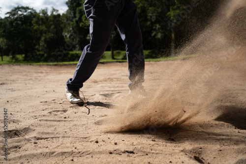 Asian golfer swings in a sand pit during pre-match practice at a golf course.