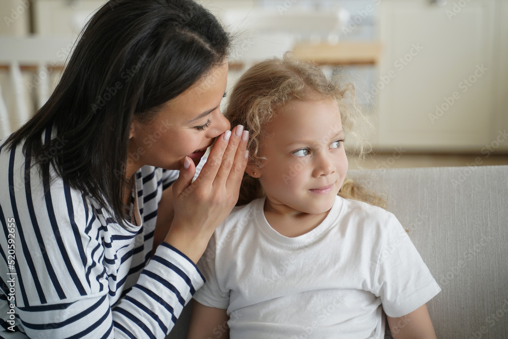 Young mom is whispering secret to little daughter. Affectionate family has happy moments together. Young mom is whispering secret to little daughter. Affectionate family has happy moments together.