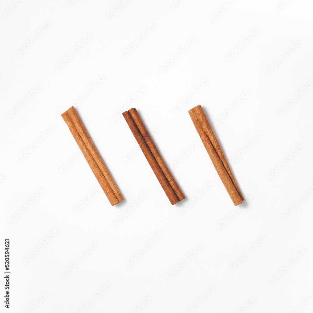 Arrangement of three cinnamon sticks arranged diagonally in the center in a flat lay. Minimalistic culinary concept in oriental style from spices for cooking and baking. Top view in square orientation
