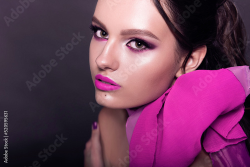 Beautiful fashionable girl haired with long curly hair posing with a pink bow. The girl in the studio on a pink background. Fashion  beauty. Bright makeup. Cosmetics for hair  healthy hair.