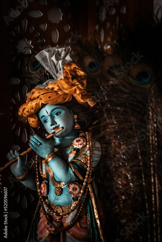 Tableau sur toile Vertical shot of a figurine of Krishna covered in gold jewllery playing on a flu