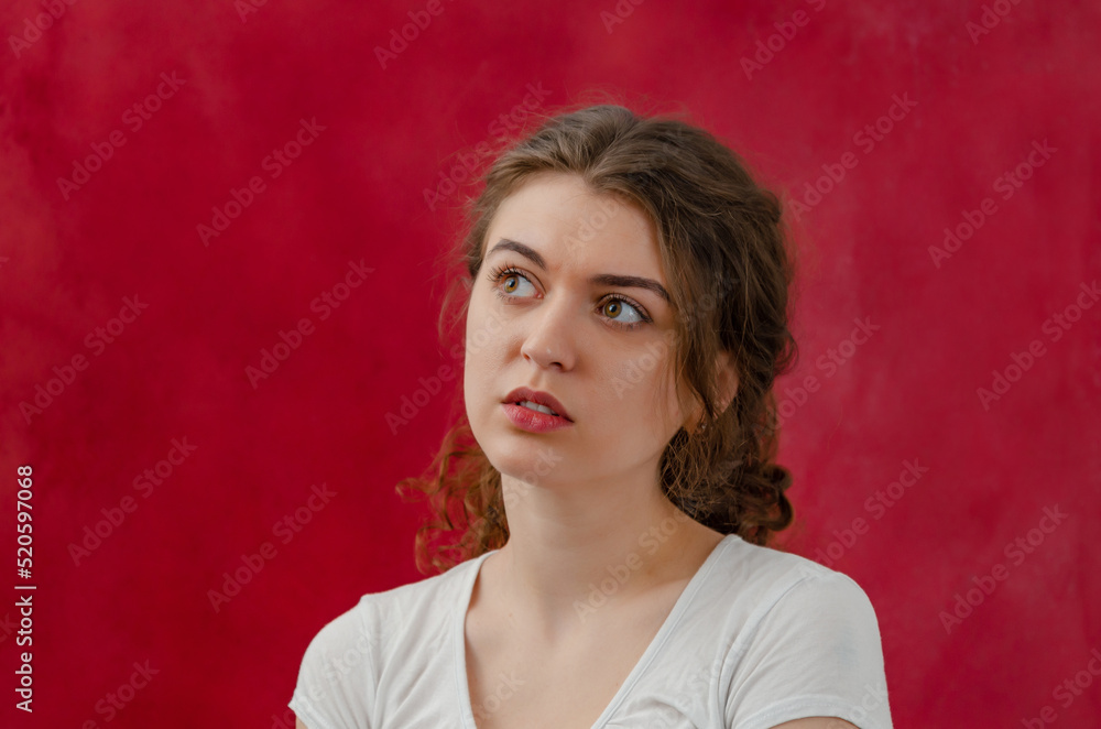 Portrait of a pensive charming young woman. Long curly dark hair. Looks to the side. Red background. Portrait of a pensive charming young woman. Long curly dark hair. Looks to the side. Red background.